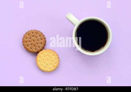 Kaffeepause flach Zusammensetzung mit braunen sandwich Cookies. Weiße heiße Tasse Kaffee und braun Dessert auf eine trendige Pastell lila Hintergrund Stockfoto