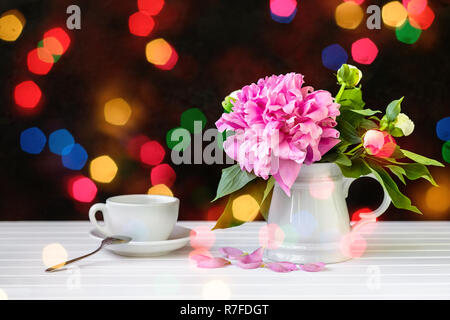 Tasse Tee und Pfingstrosen in einer Vase auf dem Tisch. Schwarzen Hintergrund. Bokeh flackern festliche Lichter. Stockfoto