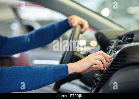 In der Nähe der Hände des Menschen in blauen Pullover. Fahrer im Auto sitzen und halten auf seine Hand auf das Lenkrad und die Heizung einschalten. Ernte von gepflegten Stockfoto