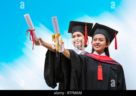 Zwei weibliche asiatischer Studierender an der Staffelung Kleid halten der Diplome Stockfoto