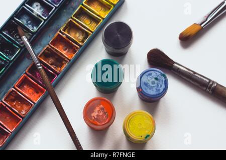 Helle und bunte Palette der Farben liegt auf weißen aquarell papier mit mehreren Bürsten für die Zeichnung. Unerlässliche Attribute für Kreativität. Stockfoto