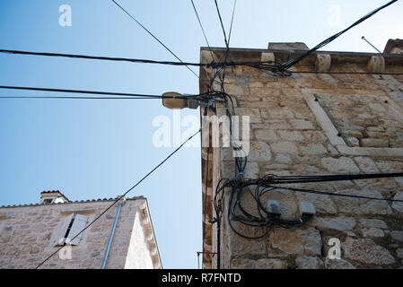 Elektrische Leitungen auf einem alten Haus aus Stein angebracht. Alte Architektur. Stromübertragung. Die Glühbirne auf dem Gebäude. Street Light Stockfoto