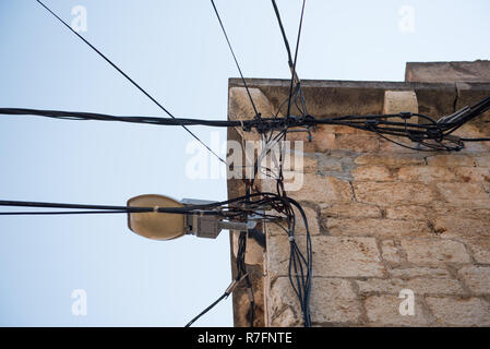 Elektrische Leitungen auf einem alten Haus aus Stein angebracht. Alte Architektur. Stromübertragung. Die Glühbirne auf dem Gebäude. Street Light Stockfoto