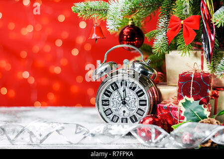 Vintage Wecker neben Geschenke und Dekorationen auf einem Holzbrett mit Schnee unter einem Weihnachtsbaum auf glänzenden Hintergrund mit Kopie Raum für t Stockfoto