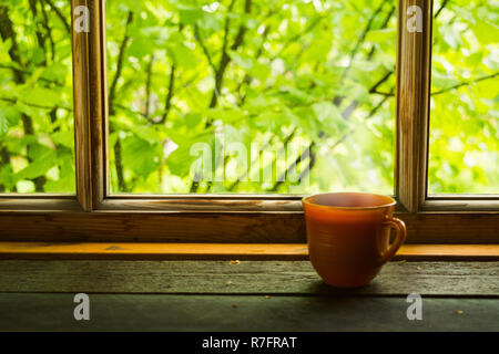 Eine Tasse heißen Getränk nea Holz- Fenster mit grünen Blättern außerhalb Stockfoto