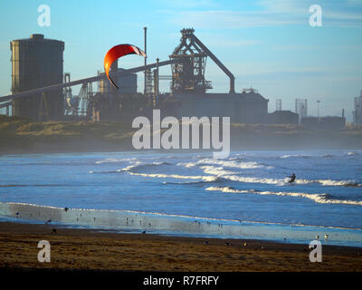 Ein Mann, Windsurfen in der Nordsee in Redcar Strand North Yorkshire mit den geschlossenen Stahlwerken hinter Stockfoto