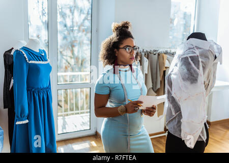 Ernsthafte curly Dame mit langen roten Ohrringe mit Bleistift und Papier Stockfoto