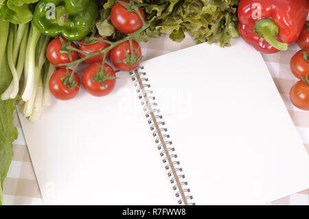 Auswahl an Salat Gemüse mit leeren Rezeptbuch oder Shopping Liste auf eine Tischdecke. Stockfoto