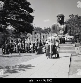 1950 histrical, japanische Touristen für ein Gruppenbild vor der grosse Buddha von Kamakura darstellen. Diese riesige Bronzestatue von Amida Buddha steht auf dem Gelände des Kotokuin Tempel, Kanagawa, Japan. Stockfoto