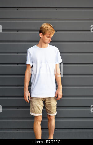 Urban mockup von Kleidung. Junge Mann stand in der Nähe der graue Metall profilierte Wand in ein weißes T-Shirt und Shorts Braun. Vorlage kann für Sie desig verwenden Stockfoto