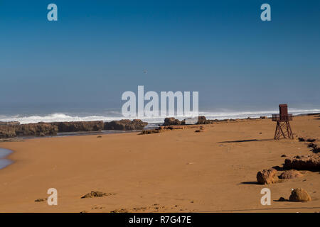 Golden sauberen Sand auf den Strand. Holz- lifeguard Tower. High Tide, Wellen mit weißen Schaum. Leeren Strand im Herbst. Horizont auf den Atlantischen Ozean. Bl Stockfoto