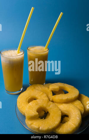 Vorderansicht zwei Gläser Ananassaft und Stücke von Ananas Obst auf den Teller, über blauer Hintergrund Stockfoto