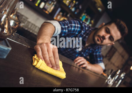 Junge Barkeeper stehen an der Theke Reinigung Oberfläche verschwommenen Hintergrund Stockfoto