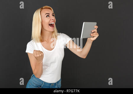 Freestyle. Frau steht auf schwarze Wand mit digitalen Tablet isoliert anschauen, lachen, glücklich, erfolgreich Stockfoto