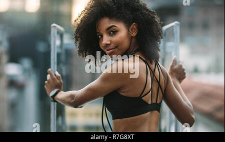 Porträt einer Frau in Fitnesskleidung, die auf dem Dach steht und beim Training arbeitet. Fitness-Frau, die auf dem Dach steht und zurückblickt. Stockfoto