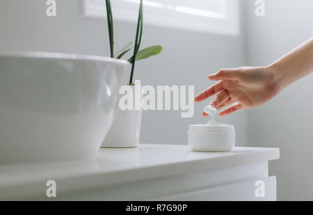 In der Nähe der weiblichen Händen, feuchtigkeitsspendende Creme von der Flasche im Bad. Frau kümmert sich um Ihre trockenen Teint. Stockfoto