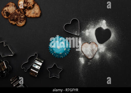 Cookies, Backformen, Papier und Süße von Zucker in Form eines Herzens auf schwarzem Hintergrund Stockfoto