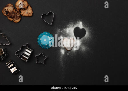 Cookies, Backformen, Papier und Süße von Zucker in Form eines Herzens auf schwarzem Hintergrund Stockfoto