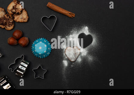 Cookies, Backformen, Schutzpapier, Zimt, Nüssen und süßem Zucker in Form eines Herzens auf schwarzem Hintergrund Stockfoto
