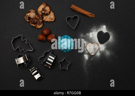 Cookies, Backformen, Schutzpapier, Zimt, Nüssen und süßem Zucker in Form eines Herzens auf schwarzem Hintergrund Stockfoto