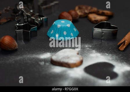 Cookies, Backformen, Schutzpapier, Zimt, Nüssen und süßem Zucker in Form eines Herzens auf schwarzem Hintergrund Stockfoto