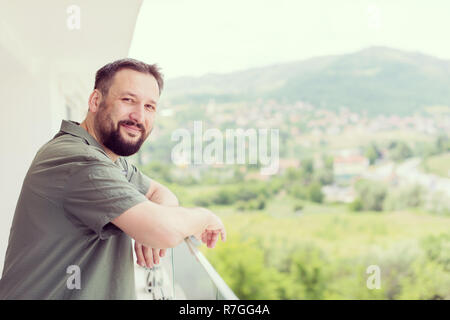 Portrait von erfolgreichen glückliche junge Hipster Mann stand auf einem modernen Balkon mit Blick auf die Stadt im Hintergrund Stockfoto