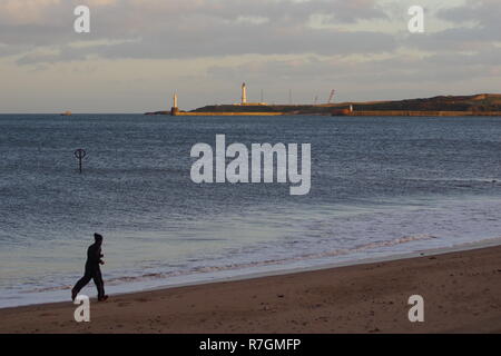 Männliche Jogger Ausübung auf Aberdeen Beach in einer ruhigen Herbstabend. Girdle Ness Leuchtturm in der Ferne. Schottland, Großbritannien. Stockfoto