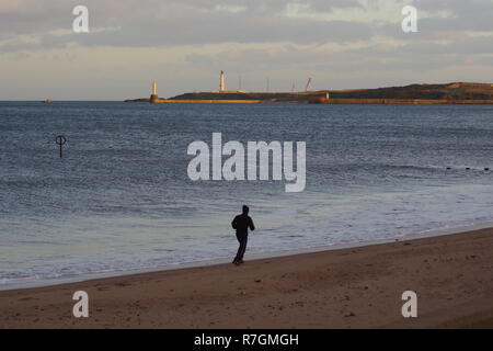 Männliche Jogger Ausübung auf Aberdeen Beach in einer ruhigen Herbstabend. Girdle Ness Leuchtturm in der Ferne. Schottland, Großbritannien. Stockfoto