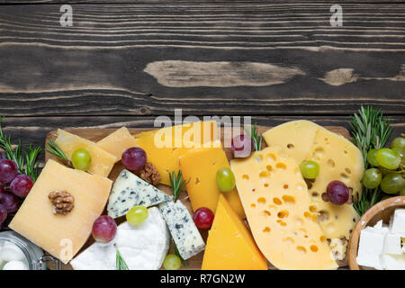 Verschiedene Käsesorten auf Holz Schneidebrett auf rustikalen Holztisch mit Trauben und Rosmarin, Ansicht von oben Stockfoto