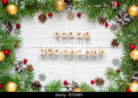 Frohe Weihnachten Beschreibung im Rahmen aus Tannenzweigen, festliche Dekorationen und Tannenzapfen auf weissem Holztisch. Weihnachten Hintergrund. Flach. t Stockfoto