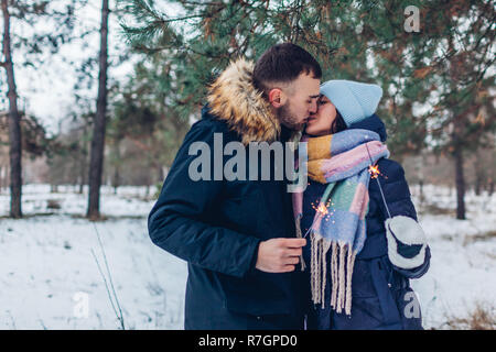 Schöne liebevolle Paar brennende Wunderkerzen und Küssen im Winter Wald. Weihnachten und neues Jahr feier Konzept Stockfoto