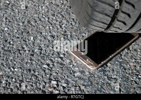 Moderne smart phone mit gebrochenen Bildschirm Glas auf dem Asphalt unter dem Auto Rad Stockfoto