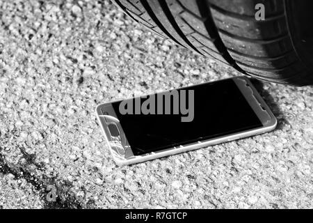 Moderne smart phone mit gebrochenen Bildschirm Glas auf dem Asphalt unter dem Auto Rad Stockfoto
