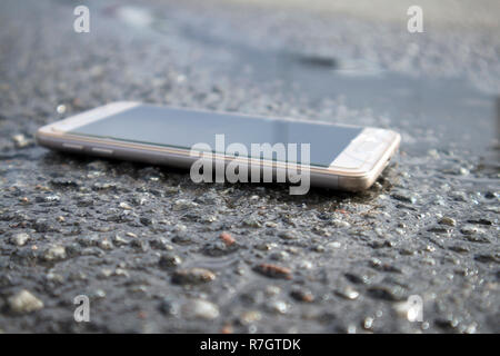 Moderne smart phone mit gebrochenen Bildschirm Glas liegen in einer Pfütze auf dem nassen Asphalt Stockfoto