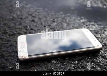 Moderne smart phone mit gebrochenen Bildschirm Glas liegen in einer Pfütze auf dem nassen Asphalt Stockfoto