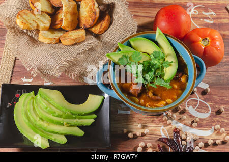 Eintopf mit Chorizo ​​and Kichererbsen, auf eine blaue Platte mit Avocado und Toast garniert mit Koriander auf einem Tisch in Low Key Licht dekoriert Stockfoto