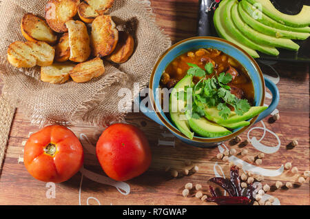 Eintopf mit Chorizo ​​and Kichererbsen, auf eine blaue Platte mit Avocado und Toast garniert mit Koriander auf einem Tisch in Low Key Licht dekoriert Stockfoto
