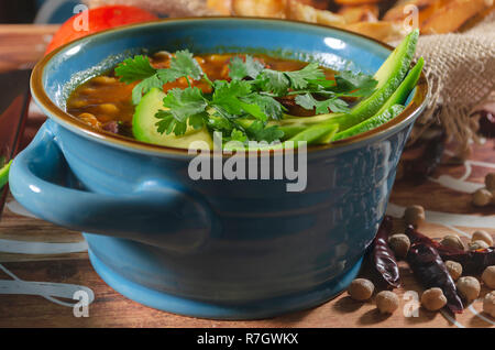 Eintopf mit Chorizo ​​and Kichererbsen, auf eine blaue Platte mit Avocado und Toast garniert mit Koriander auf einem Tisch in Low Key Licht dekoriert Stockfoto
