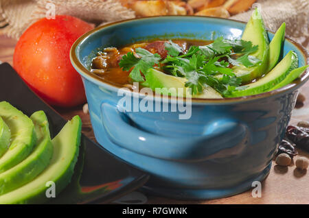 Eintopf mit Chorizo ​​and Kichererbsen, auf eine blaue Platte mit Avocado und Toast garniert mit Koriander auf einem Tisch in Low Key Licht dekoriert Stockfoto