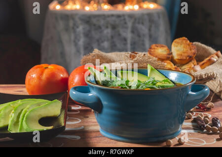 Eintopf mit Chorizo ​​and Kichererbsen, auf eine blaue Platte mit Avocado und Toast garniert mit Koriander auf einem Tisch in Low Key Licht dekoriert Stockfoto