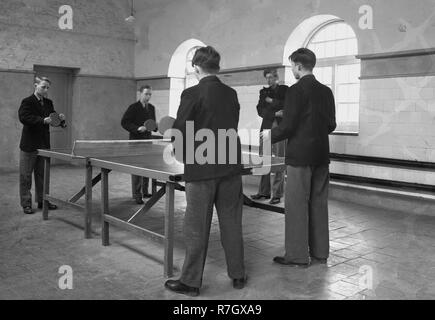 1950, historische, vier Internat Jungen in ihren einheitlichen drinnen spielen Sie eine Partie Tischtennis oder Ping pong, England, UK. Stockfoto