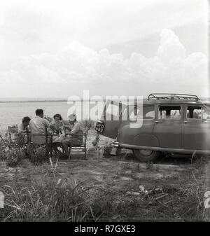 1950 s, Uganda, Afrika, britischen Leuten an einem Tisch sitzen bei einem Picknick neben ihrem Auto am Ufer des Lake Victoria. Stockfoto