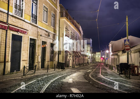 Eine Straße mit Bürgersteig mit Straßenbahn Eisenbahnen in einer stürmischen Nacht leer von Menschen in Lissabon, Portugal. Stockfoto