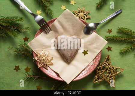 Weihnachtsdekoration mit Lebkuchenherz auf einem Teller, kleine goldene Sterne und Zweige Fichte um Stockfoto