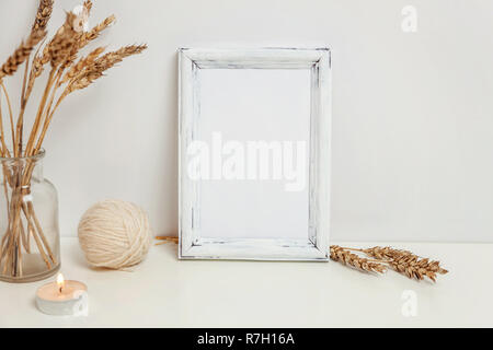 Vertikale Rahmen mockup mit wilden Roggen Blumenstrauß in glass vase in der Nähe von weißen Wand. Leeren Rahmen mock up für Presentation Design. Vorlage framing für moderne Ar Stockfoto