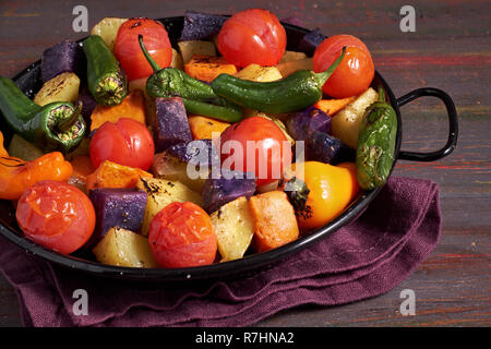 Rustikal, Ofen gebackenes Gemüse in Auflaufform. Saisonale vegetarische vegane Mahlzeit auf dunklem Hintergrund mit Bettwäsche Handtuch. Zutaten: Kartoffeln, Violett Stockfoto