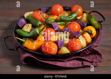 Rustikal, Ofen gebackenes Gemüse in Auflaufform. Saisonale vegetarische vegane Mahlzeit auf dunklem Hintergrund mit Bettwäsche Handtuch. Zutaten: Kartoffeln, Violett Stockfoto