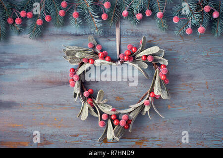 Heart-shaped Mistel Weihnachten Kranz und festliche Girlande aus Tannen Zweigen und Frosted Beeren auf rustikalen Holzmöbeln Hintergrund Stockfoto