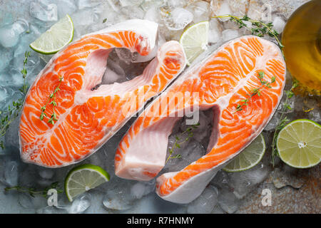 Zwei rohe frische Lachs oder Forelle Steaks auf Eis, die reich an Omega-3-Öl, mit Kalk, Thymian und Olivenöl auf einem blauen Hintergrund rostig. Gesunde und diätetische Lebensmittel. Stockfoto