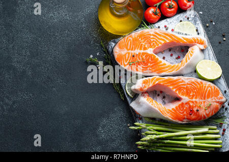 Zwei rohe frische Lachs oder Forelle Steaks, reich an Omega-3 Öl, mit Kalk, Thymian und Olivenöl auf einem dunklen Hintergrund. Gesunde und diätetische Lebensmittel. Ansicht von oben wit Stockfoto